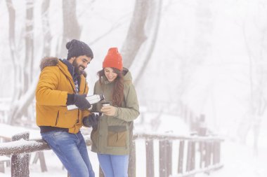 Güzel, genç ve aşık bir çift, kar yağışlı bir kış gününde dışarıda dinlenirken, sıcak çay içerek ve yürüyüş molası vererek ısınıyorlar. 