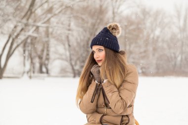 Çekici sarışın, kışlık kıyafetler giyiyor, atkısını tutuyor ve doğada güzel bir kış gününün tadını çıkarıyor.