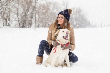 Güzel genç bir kadın karda köpeğine sarılıyor.