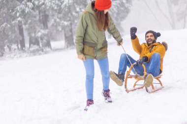 Çiftler kış tatillerini dağlarda geçiriyorlar, karlı bir günü dışarıda geçiriyorlar, kadınlar erkekleri kızakla çekiyor.