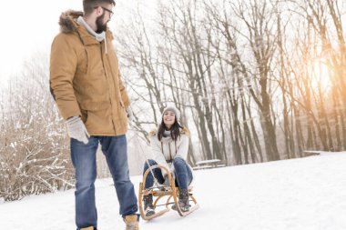 Güzel genç bir çift bir kış tatil zevk ve karlı kış gününde eğleniyor aşık. Erkek arkadaşı bir kızak üzerinde çekerek