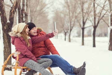 Kış tatilinde aşık olan genç bir çift kızakta oturup selfie çekiyorlar.