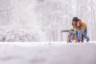 Güzel, genç bir çift, dağlarda bir kış tatilinde eğleniyor, erkek arkadaş, kız arkadaşını kızağa itiyor, karlı, sisli kış gününün tadını çıkarıyor.