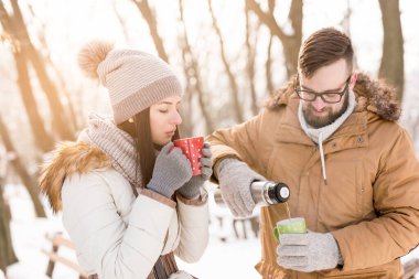 Güzel, genç ve aşık bir çift kış tatilinin tadını çıkarıyor, karda sıcak çay içiyor ve içiyorlar. Kıza odaklan.