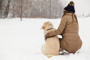 Genç bir kadın kameraya bakmadan köpeğine sarılıyor.