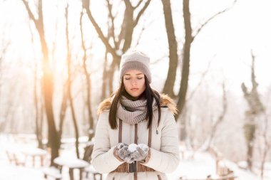 Güzel genç bir kadın güneşli bir kış gününün tadını çıkarıyor ve karda oynarken eğleniyor.