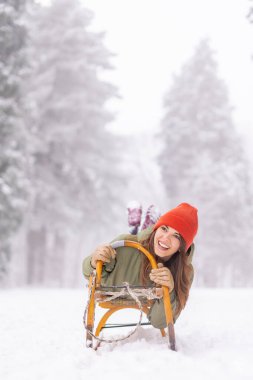 Güzel genç bir kadın kızakta uzanıyor. Dağlarda kış tatili yaparken tepeden aşağıya kayarak eğleniyor.