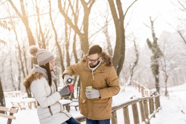 Birbirine aşık bir çift kış tatilinde karda dikiliyor, sıcak çay içiyor ve dağlarda karlı kış gününün tadını çıkarıyor.