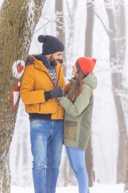 Birbirine aşık bir çift, karlı bir kış gününde el ele tutuşup ormanda yürüyüş yapıyor, dağlarda kış tatilinin tadını çıkarıyor.