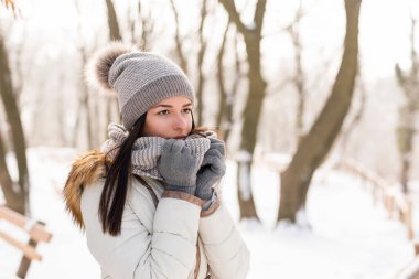 Güzel genç bir kadın ciddi ve düşünceli duruyor, atkısını tutuyor, güzel bir kış gününün tadını çıkarıyor.