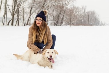 Güzel genç bir kadın köpeğine sarılıyor ve karlı bir kış gününün tadını çıkarıyor.