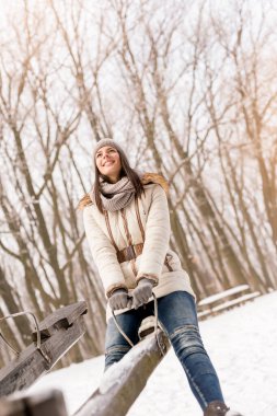 Güzel genç bir kadın tahterevallide oturuyor, kış tatilinde eğleniyor, açık havada karlı kış gününün tadını çıkarıyor.