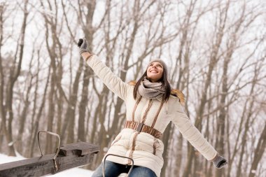 Güzel genç bir kadın tahterevallide oturuyor, eğleniyor ve karlı kış gününün tadını çıkarıyor.