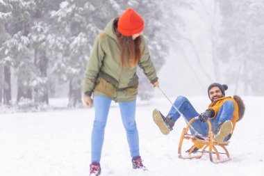 Çiftler kış tatillerini dağlarda geçiriyorlar, karlı bir günü dışarıda geçiriyorlar, kadınlar erkekleri kızakla çekiyor.