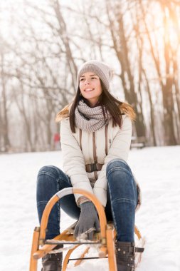 Güzel kız kızakta oturuyor ve karlı bir kış gününün tadını çıkarıyor.