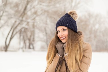 Çekici sarışın, kışlık kıyafetler giyiyor, atkısını tutuyor ve doğada güzel bir kış gününün tadını çıkarıyor.