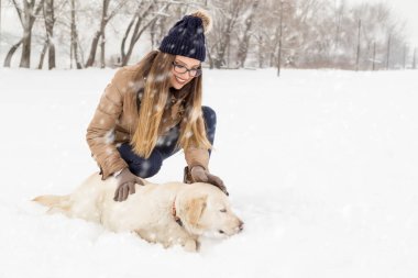 Güzel genç bir kadın köpeğine sarılıyor ve karlı bir kış gününün tadını çıkarıyor.