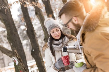 Birbirine aşık bir çift kış tatilinde karda duruyor, sıcak çay içiyor ve karlı kış gününün tadını çıkarıyor.