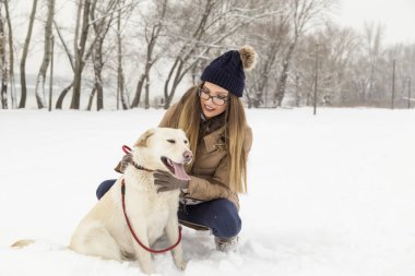 Güzel genç bir kadın köpeğiyle karda oynuyor, doğada güzel bir kış gününün tadını çıkarıyor.