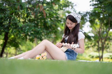 Genç Asyalı kadın parkta Ukulele çalarak eğleniyor ve dinleniyor. Müzik zamanı.