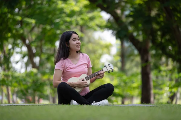 Asyalı sağlıklı hamile kadın parkta Ukulele oynayarak, anne sağlığı ve müzik yaparak eğleniyor ve dinleniyor.