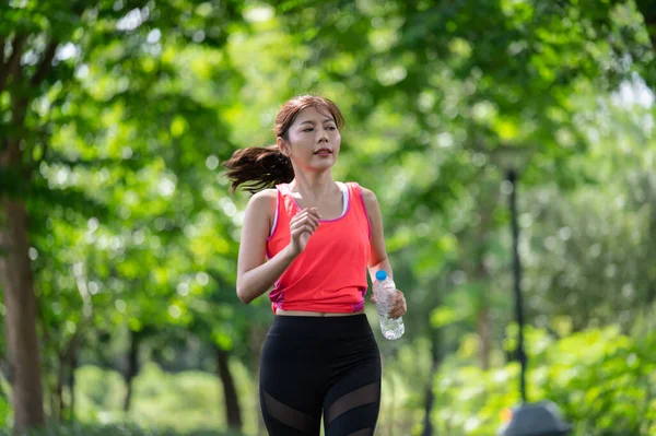 快乐的亚洲女赛跑选手在街上跑来跑去 在公园里拿着水瓶 图库照片