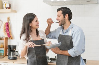Mutlu genç çift evdeki mutfak tezgahında birlikte yemek pişiriyor.