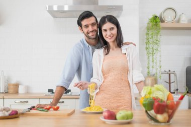 Mutlu genç çift evdeki mutfak tezgahında birlikte yemek pişiriyor.