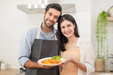 Mutlu çift evde yemek hazırlıyor, genç çift mutfak tezgahında sebze kesiyor, aşık erkek ve kadın.