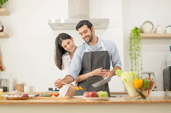 Happy couple preparing food at home, young couple cutting vegetables together at kitchen counter, man and woman in love