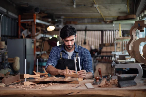 Luthier bir gitar yaratıyor ve geleneksel olarak aletleri kullanıyor. Yapım aşamasında olan bir gitarın gövdesine kelepçe takıyor. Yapıştırıcı yapışkanlığını geliştiriyor.