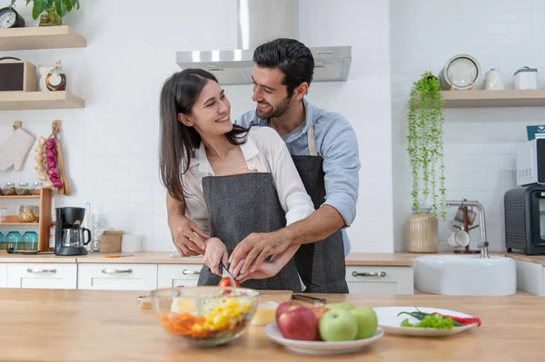 Happy couple preparing food at home, young couple cutting vegetables together at kitchen counter, man and woman in love