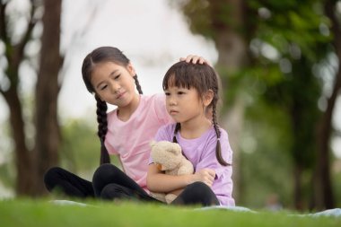 Asyalı aile çocukları ablası küçük kız kardeşini parkta teselli ediyor.