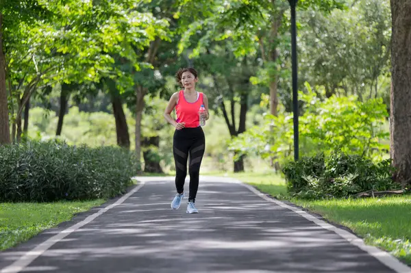 Happy Asian female runner running on the street outdoors in the park