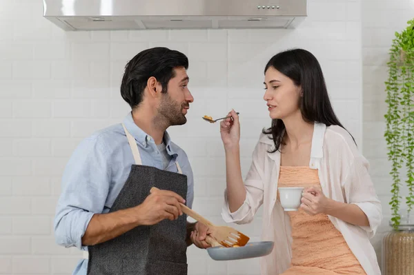 Happy young couple cooking together in the kitchen counter, feeding each other in their kitchen at home