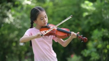 Parkta keman çalan tatlı Asyalı küçük kız, eğitim müziği konsepti.