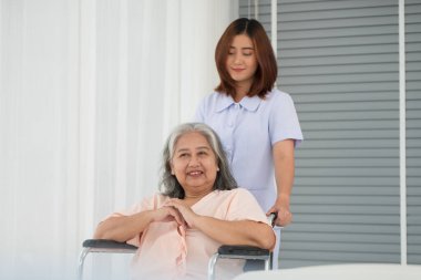 Hastane koğuşunda yaşlı kadın hastayı tekerlekli sandalyeye iten Asyalı hemşire, yaşlı bakım konsepti