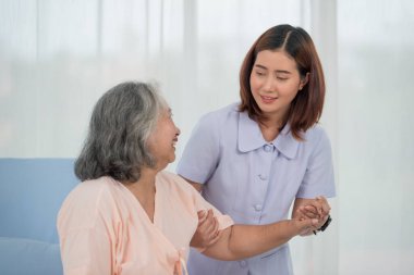 Gülümseyen Asyalı doktor, klinikte ya da hastanede yatağında yatan yaşlı kadın hastanın elini tutuyor. Yaşlılar sağlık hizmeti kavramı.