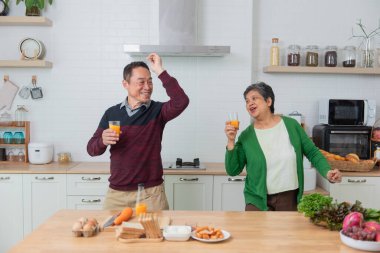 Mutlu Asyalı son sınıf çifti modern mutfakta taze meyve suyu içiyor, sağlıklı yiyecekler.