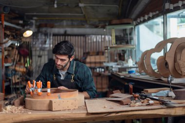 Luthier creating a guitar and using tools in a traditional, clamps on the body of a guitar under construction improving glue adhesion clipart