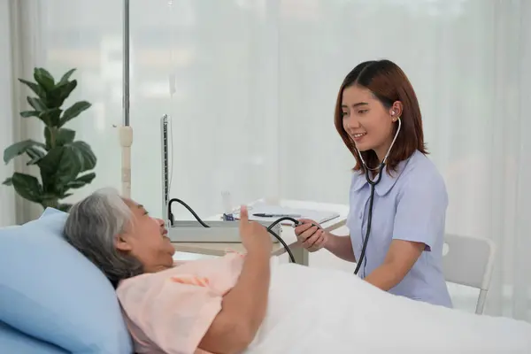 Asian nurse with tonometer measuring senior woman patient\'s blood pressure at hospital