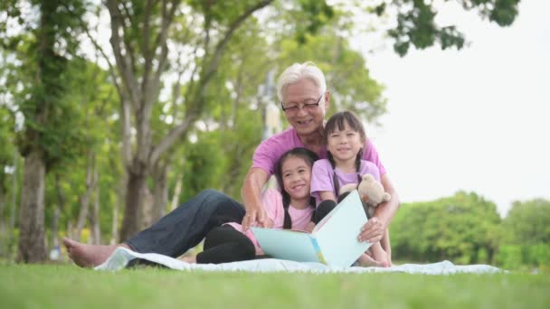 公園で祖父と本を読んでいる幸せなアジアの家族の子供たち — ストック動画