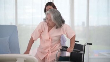 Hastane koğuşunda yaşlı kadın hastayı tekerlekli sandalyeye iten Asyalı hemşire, yaşlı bakım konsepti