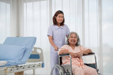 Hastane koğuşunda yaşlı kadın hastayı tekerlekli sandalyeye iten Asyalı hemşire, yaşlı bakım konsepti
