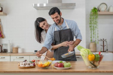 Mutlu çift evdeki mutfak tezgahında yemek pişiriyor ve sarılıyorlar.