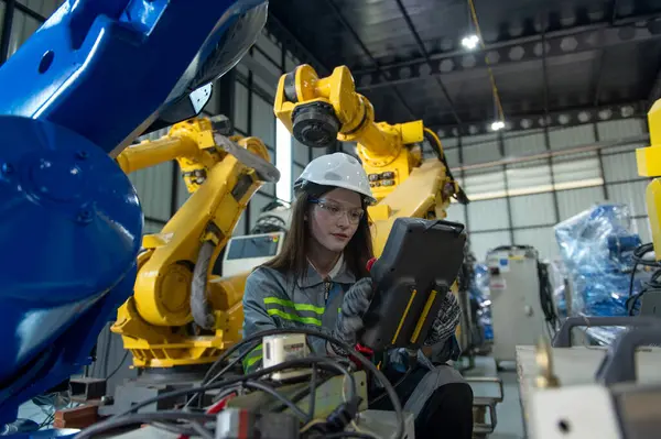 Kask güvenlik işçisi olan mühendis kadın endüstri fabrikasında robot kolla çalışıyor.