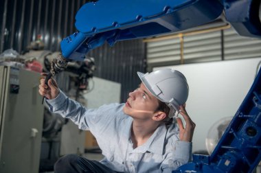 Robotik kol ve işletim makinesinin yanında duran miğfer güvenlikli mühendis. Teknisyen, tamir onarım elektronik işlemleri için kontrol ediyor.