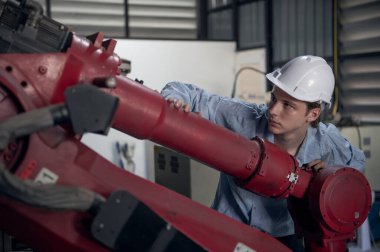 Robotik kol ve işletim makinesinin yanında duran miğfer güvenlikli mühendis. Teknisyen, tamir onarım elektronik işlemleri için kontrol ediyor.