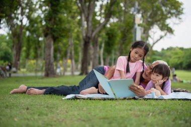 Mutlu Asyalı aile çocukları büyükbabasıyla parkta kitap okuyor.