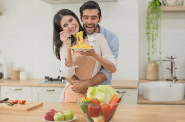 Mutlu genç çift mutfak tezgahında birlikte yemek pişiriyor, evlerinde birbirlerini besliyorlar.